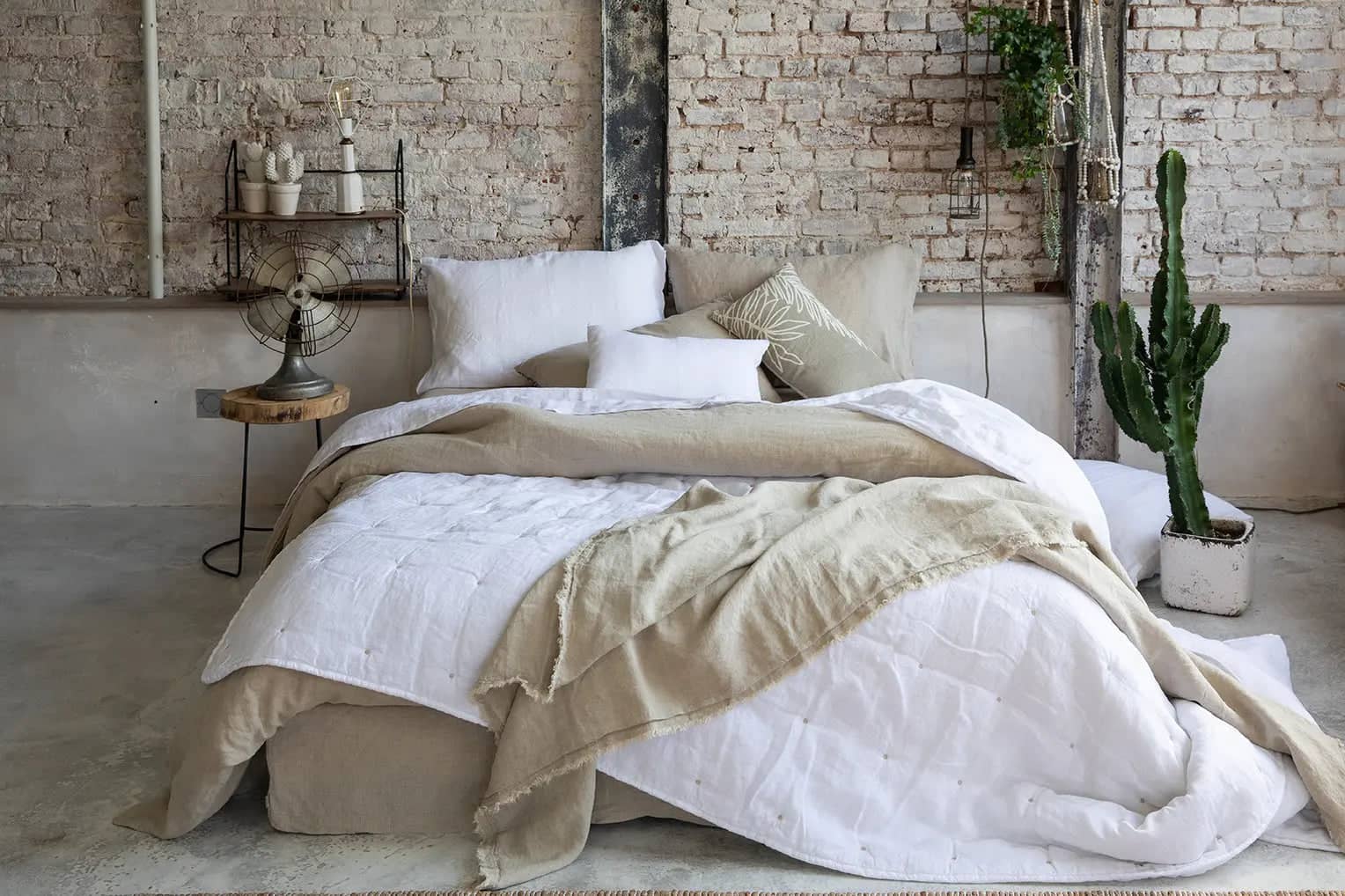Chambre avec lit décoré d'un jeté de lit en lin beige sur une couverture blanche dans un style industriel
