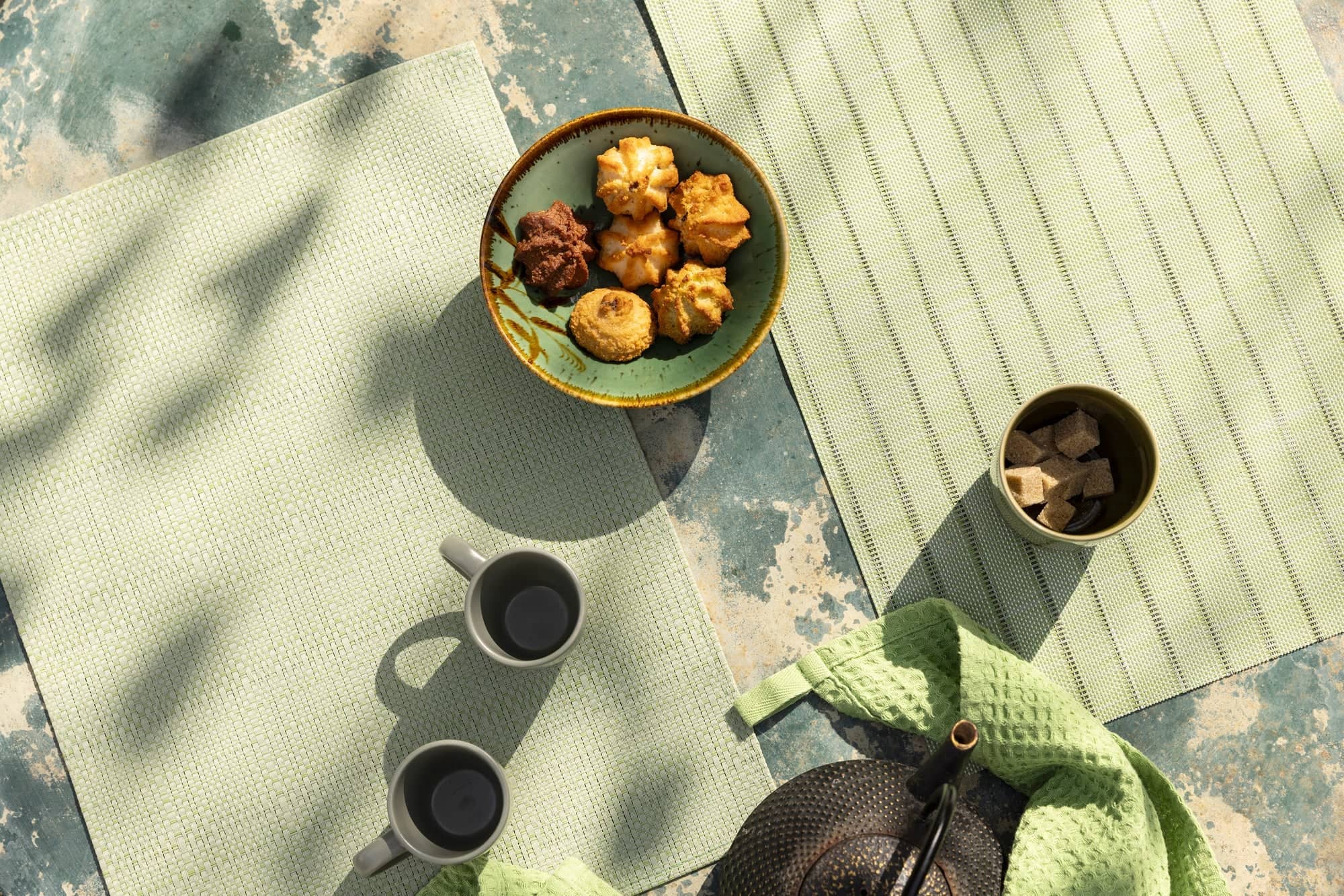Set de table pvc tissé en vert clair avec théière, tasses et biscuits sur une table rustique