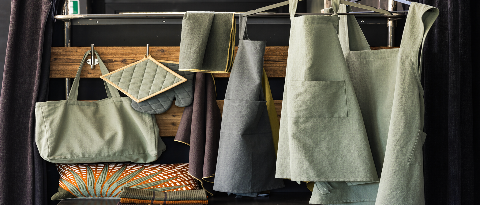 Collection de tablier coton de qualité suspendus avec accessoires de cuisine gris et verts dans un intérieur moderne