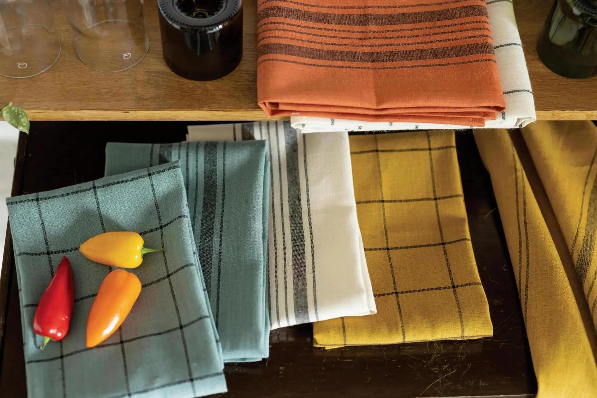 Collection de linge de cuisine en lin coloré avec motifs à carreaux et poivrons sur une table en bois