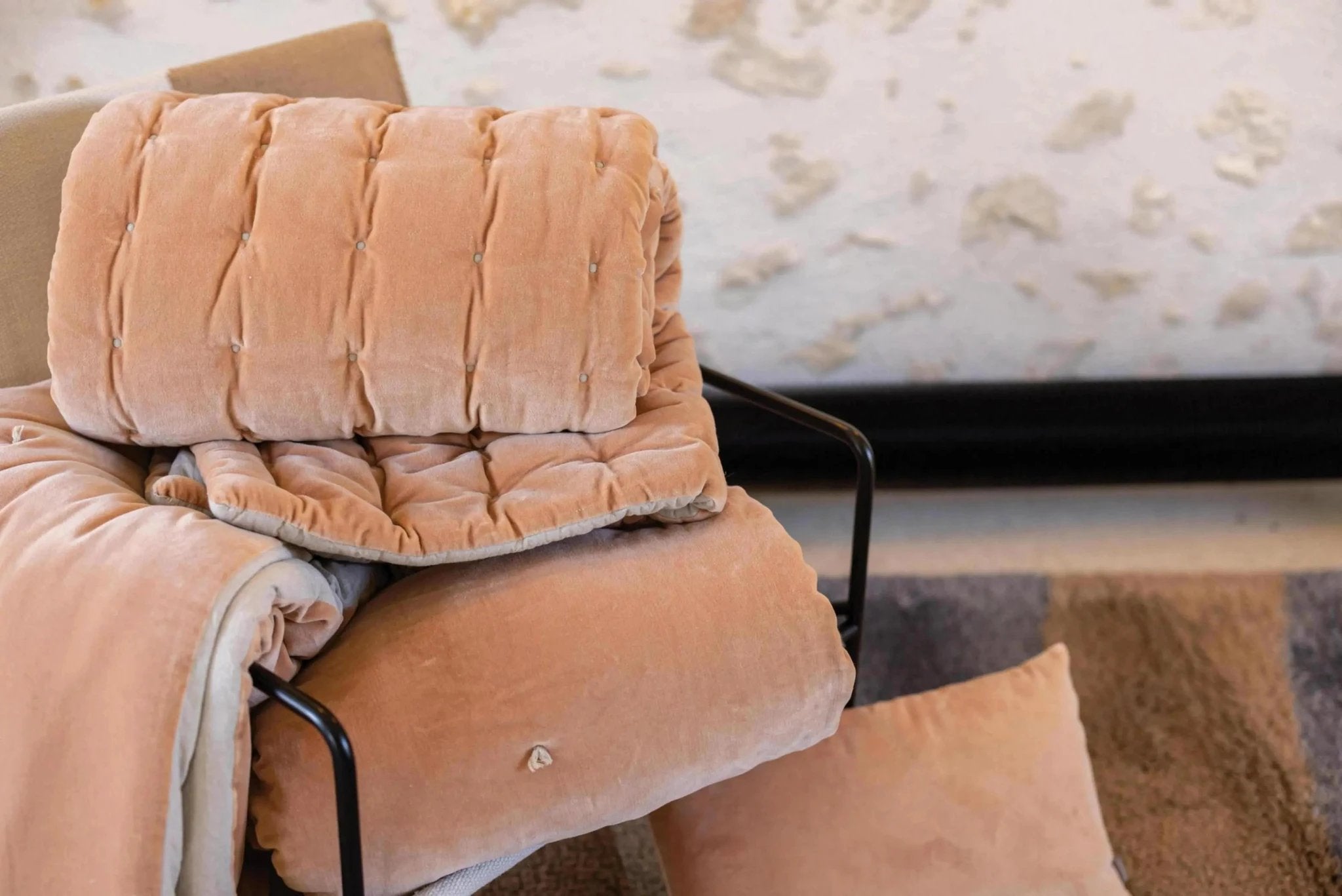 Chemin de lit Vivaraise en tissu velours beige doux et moelleux posé sur un fauteuil noir