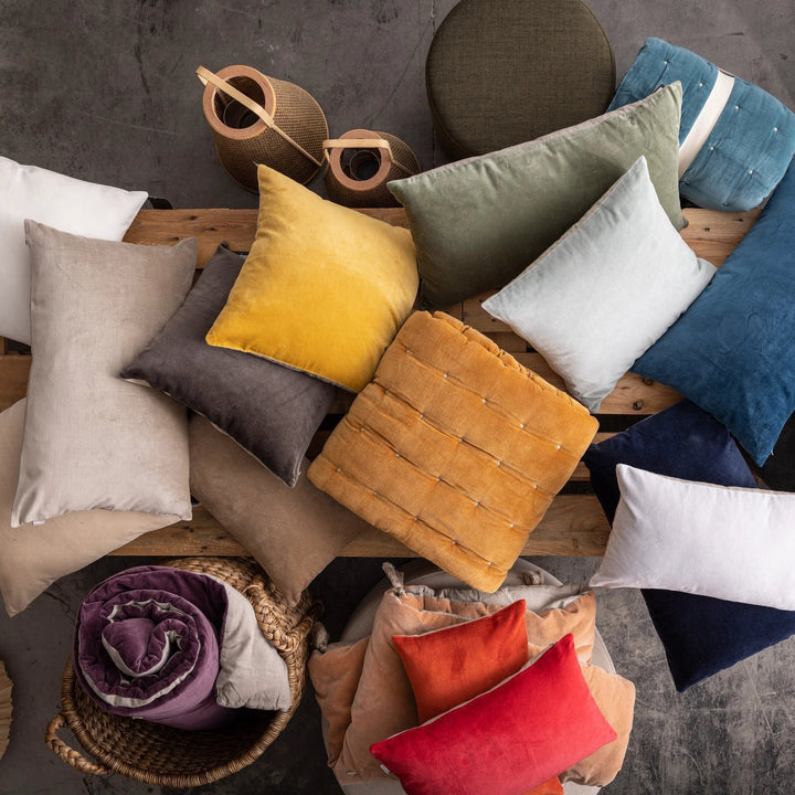 Collection de coussins décoratifs en velours de différentes couleurs sur un banc en bois