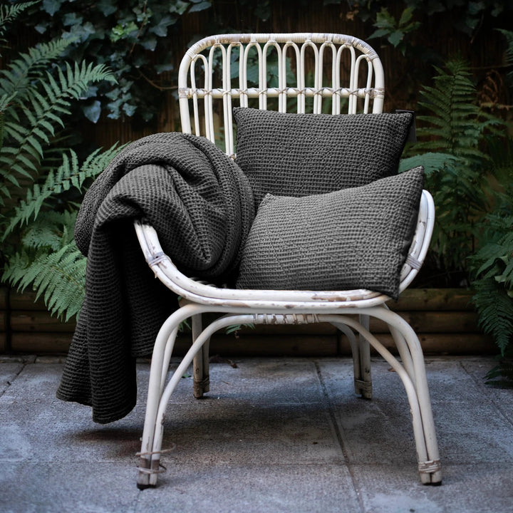 Chaise en rotin avec coussins décoratifs gris et plaid tricoté par Vivaraise pour décoration intérieure