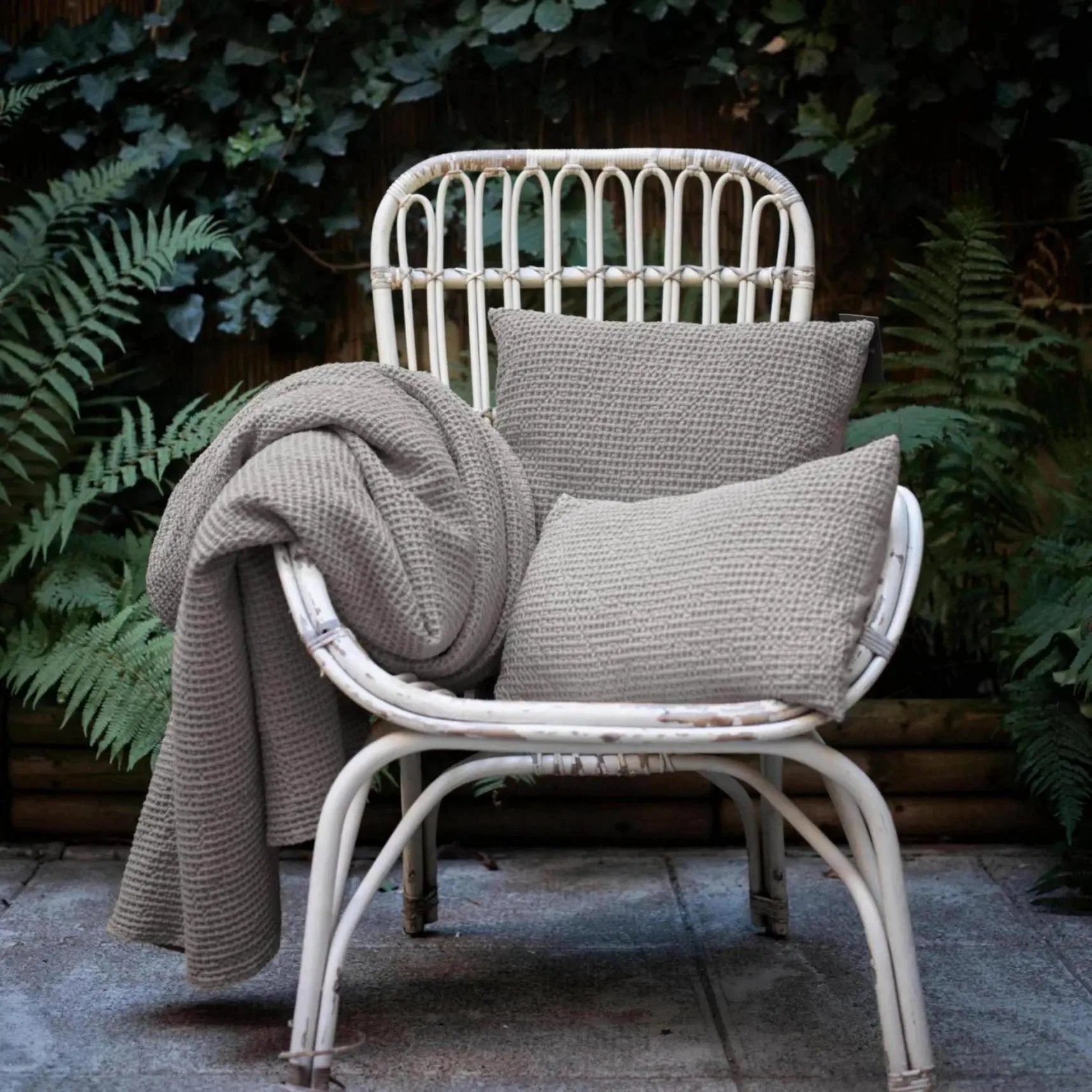 Coussins décoratifs gris posés sur une chaise en rotin blanc avec couverture assortie Vivaraise