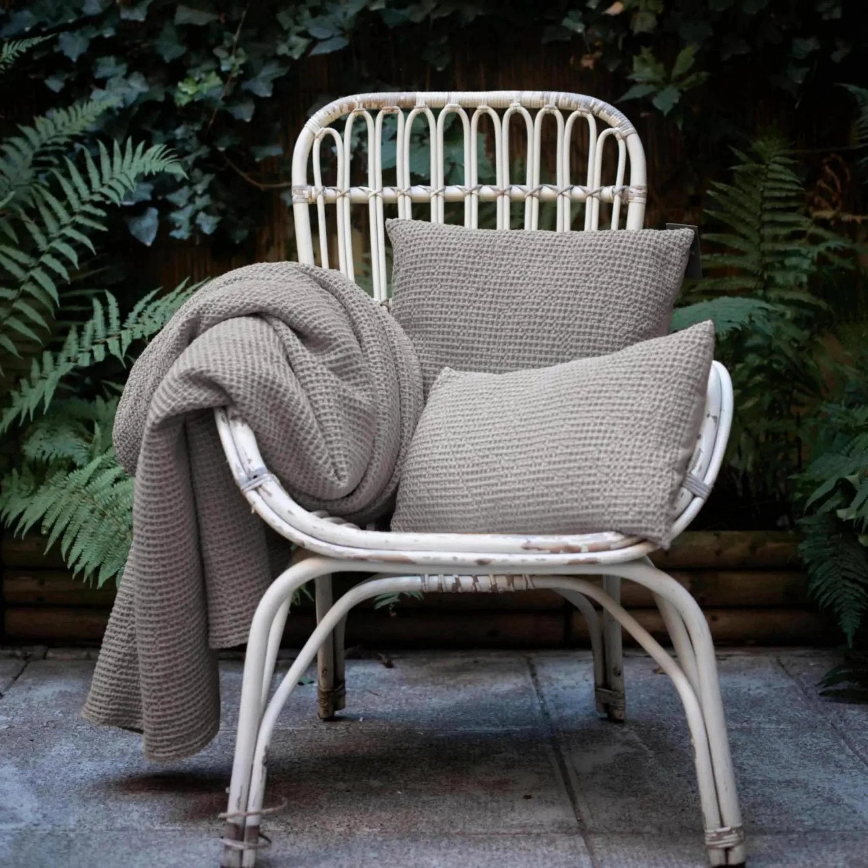 Chaise en rotin blanc avec coussins décoratifs beige et couverture texturée en extérieur