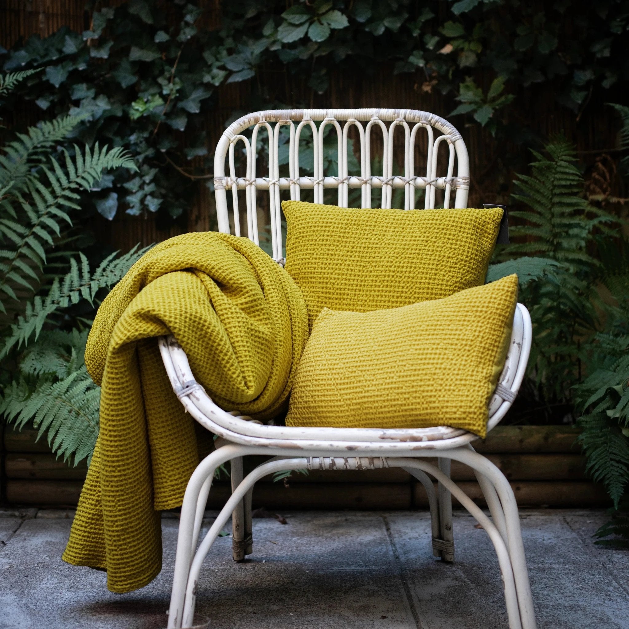 Coussin décoratif jaune Vivaraise sur une chaise en rotin avec couverture assortie