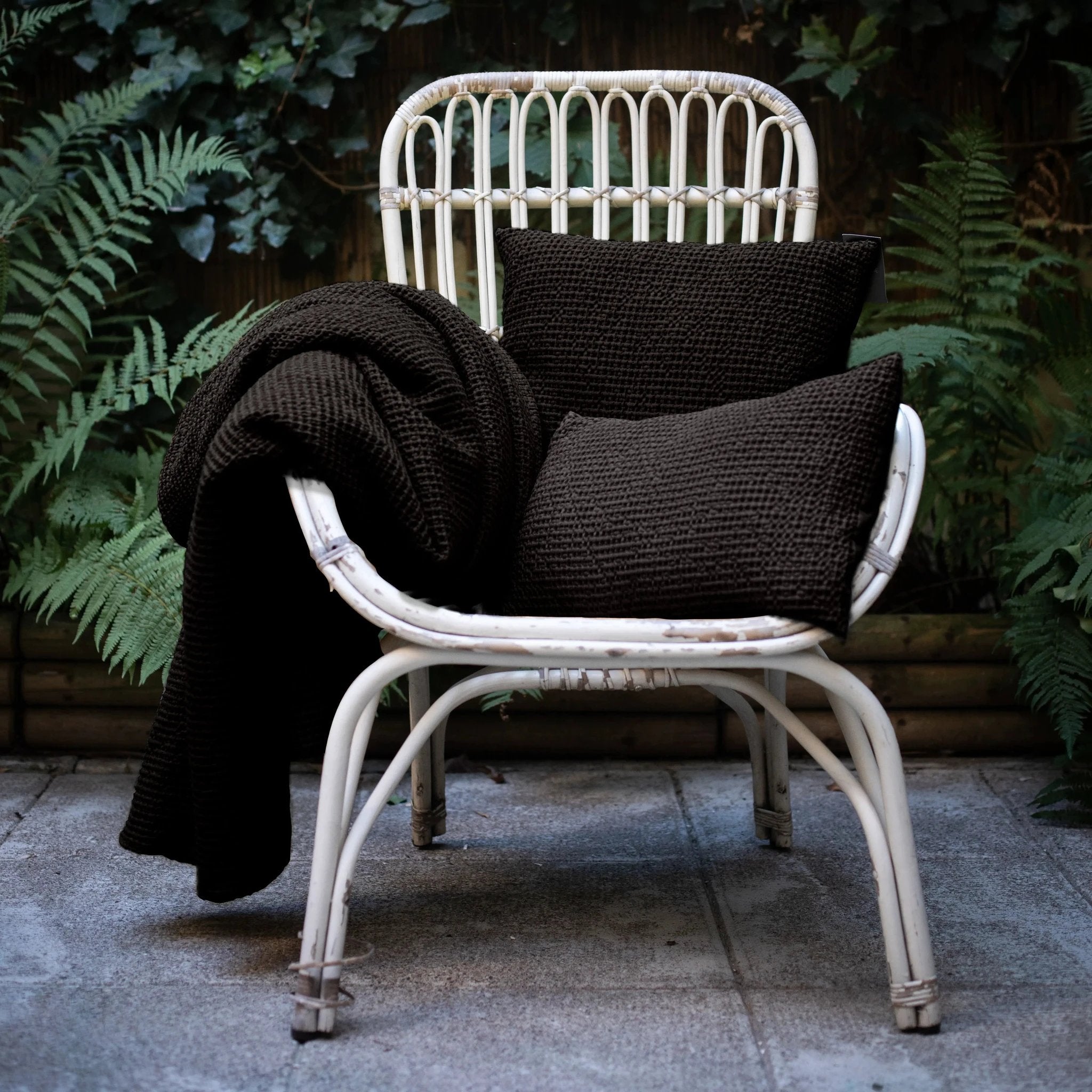 Chaises en rotin blanc avec coussins décoratifs jaunes et couverture noire dans un jardin
