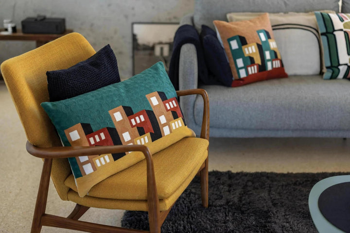 Plaid Vivaraise avec motif de maisons colorées posé sur un fauteuil jaune dans un salon moderne