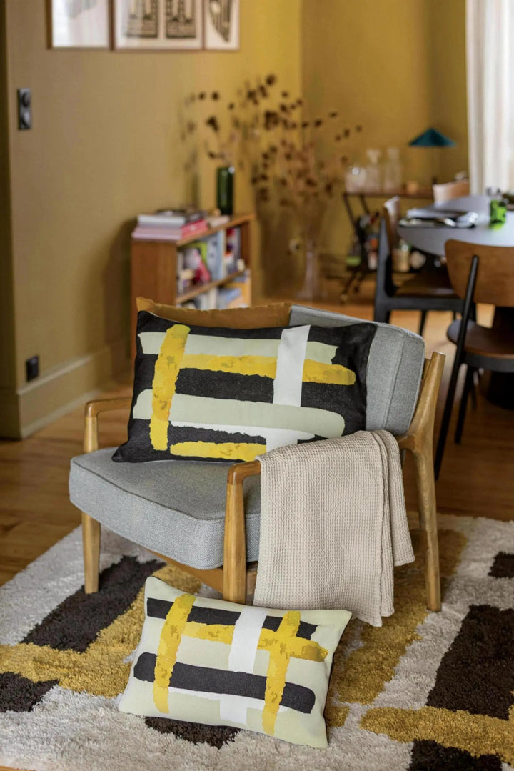 Plaid beige Vivaraise posé sur un fauteuil en bois avec coussins graphiques dans un salon moderne
