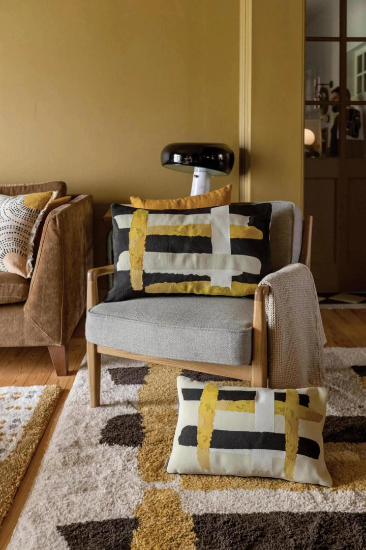 Plaid Vivaraise décoratif avec motifs noirs, blancs et jaunes sur fauteuil gris en salon moderne