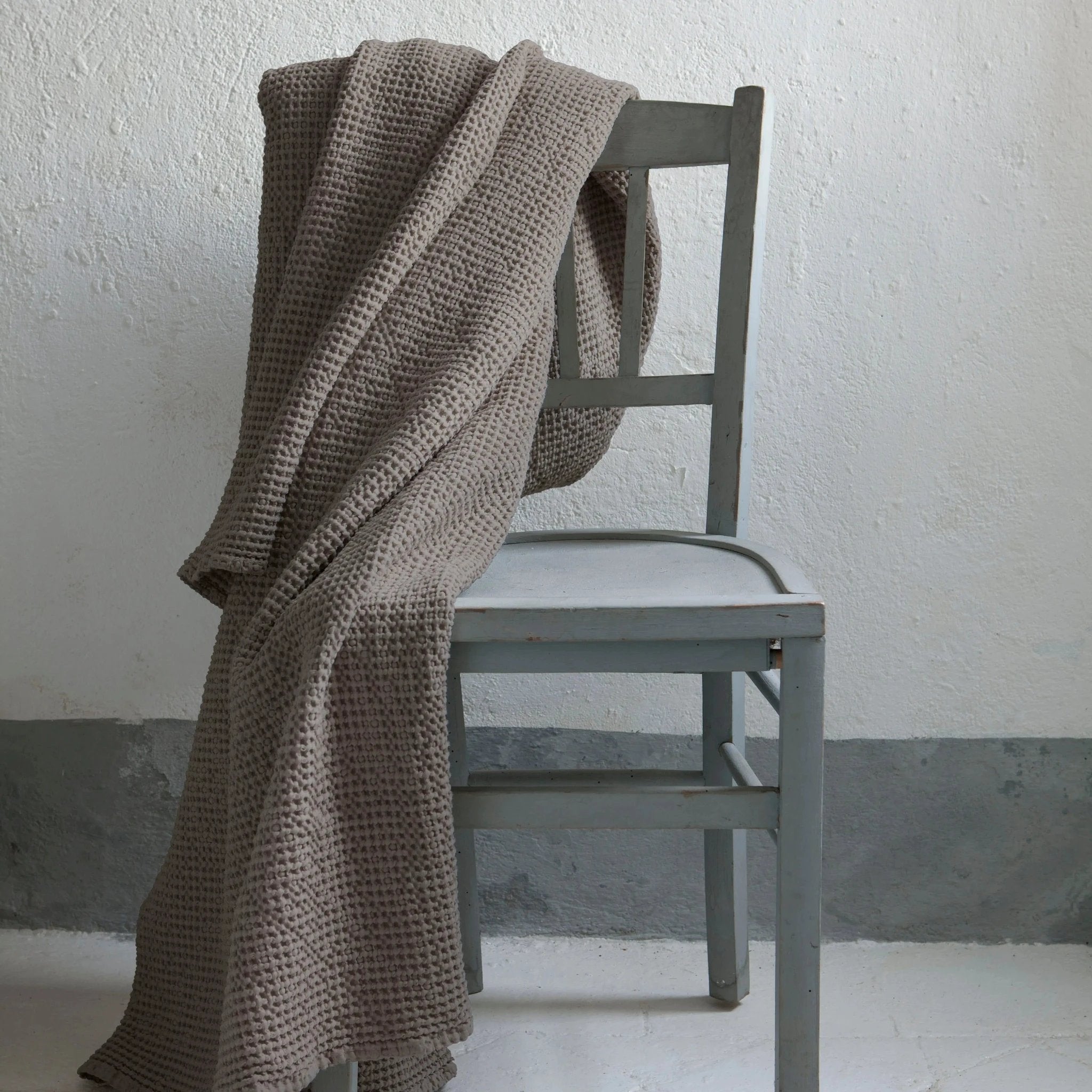 Plaid beige en texture gaufrée drapé sur une chaise en bois gris de Vivaraise