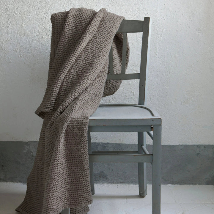 Plaid beige en texture gaufrée drapé sur une chaise en bois gris de Vivaraise